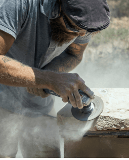 Man using a grinder to cut or shape rock at a construction site