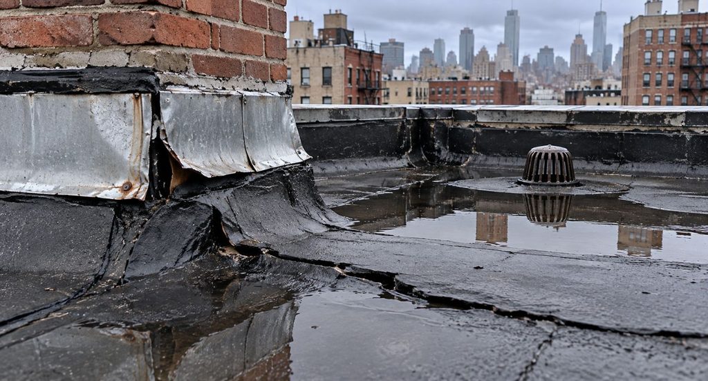 Damaged flashing, cracked roof membrane, and standing water on an NYC flat roof