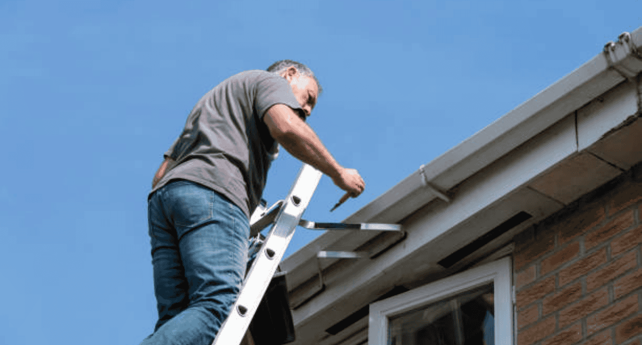 Technician repairing roof gutter on ladder, home exterior roofing service and maintenance work in progress