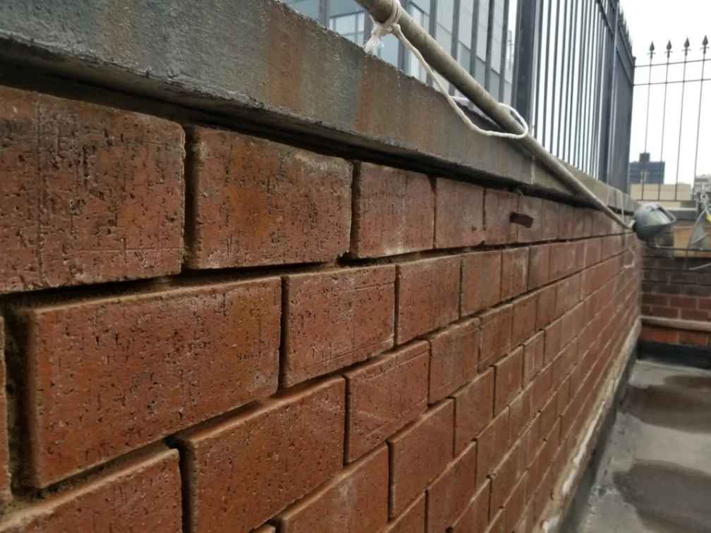 Nuera inspection of uneven brick parapet wall with visible gaps and alignment defects.